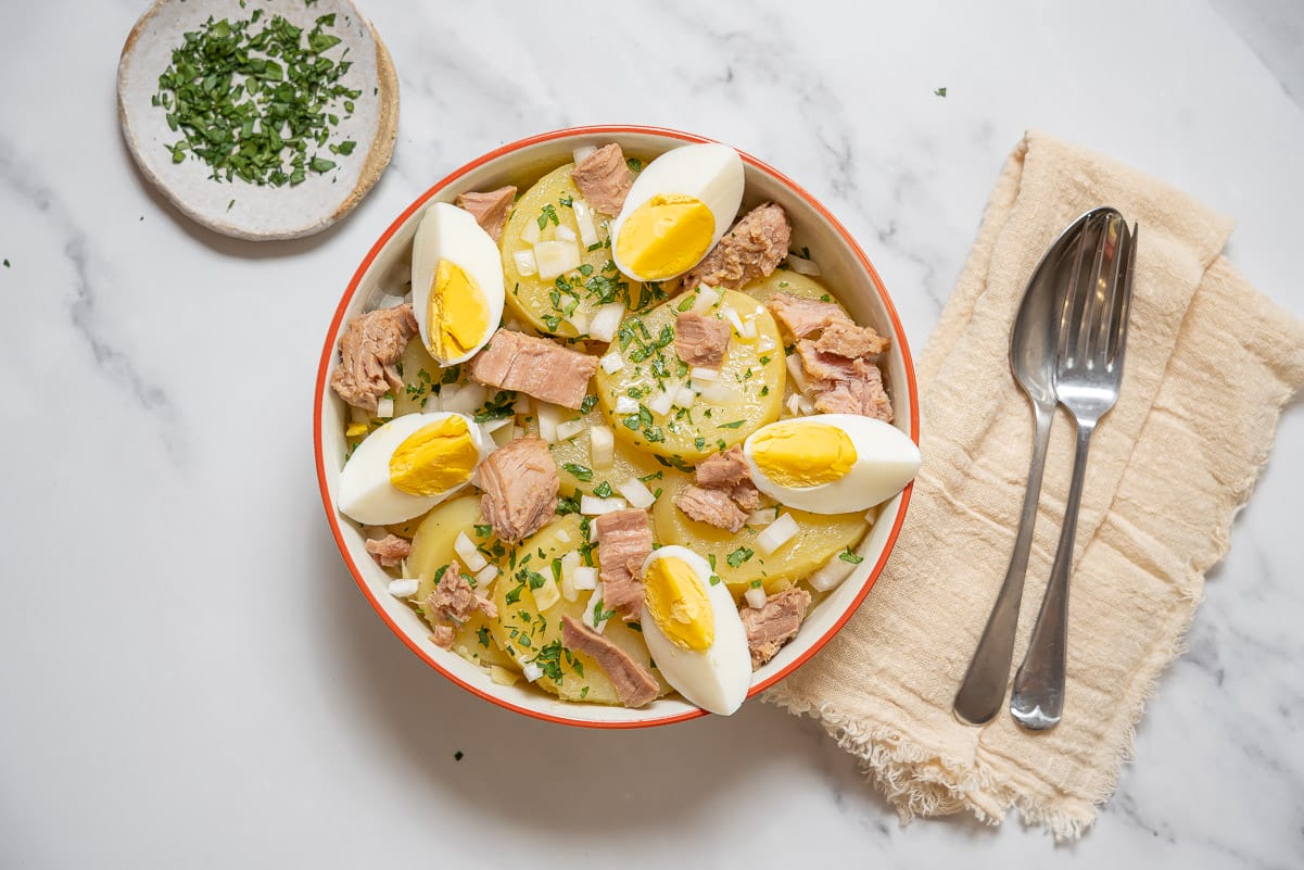 bowl of sliced potatoes topped with boiled egg and tuna.