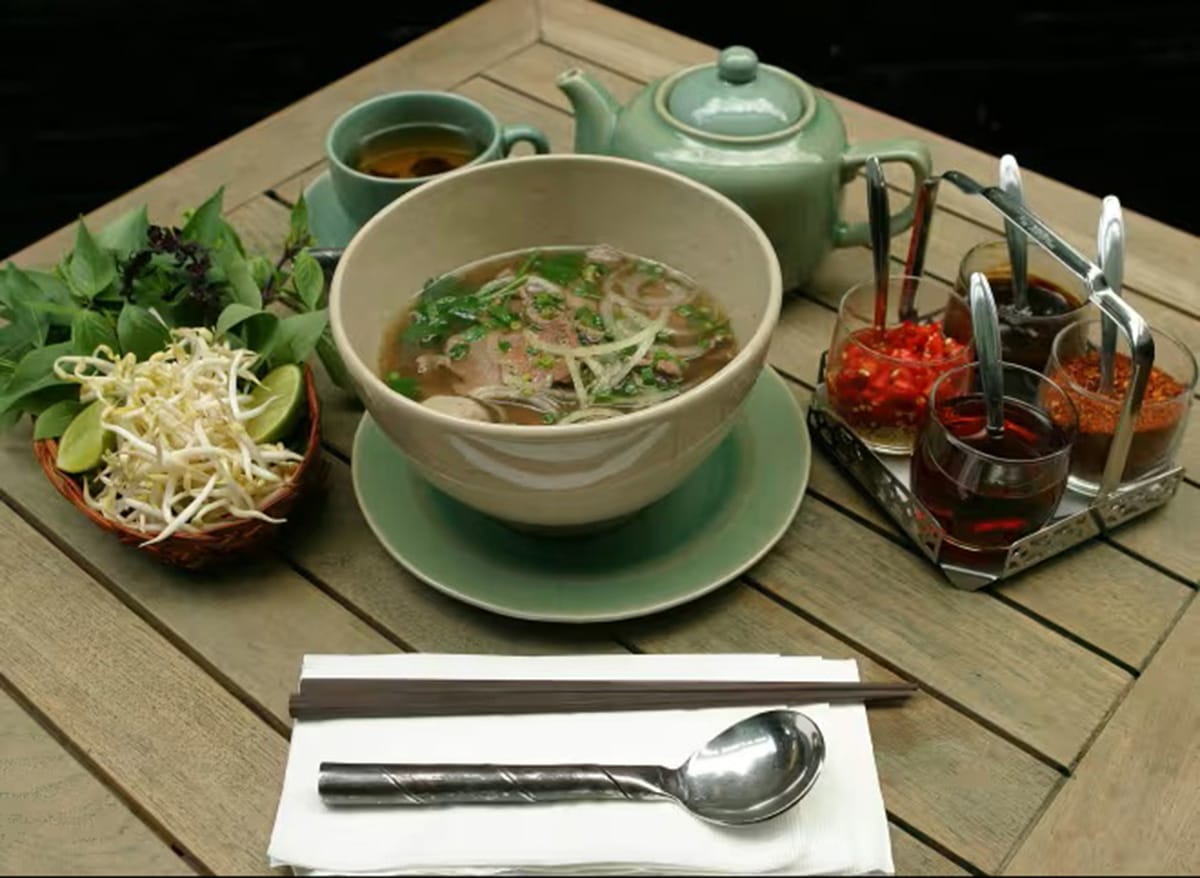bowl of pho with a cup of tea and a teapot with four sauces.