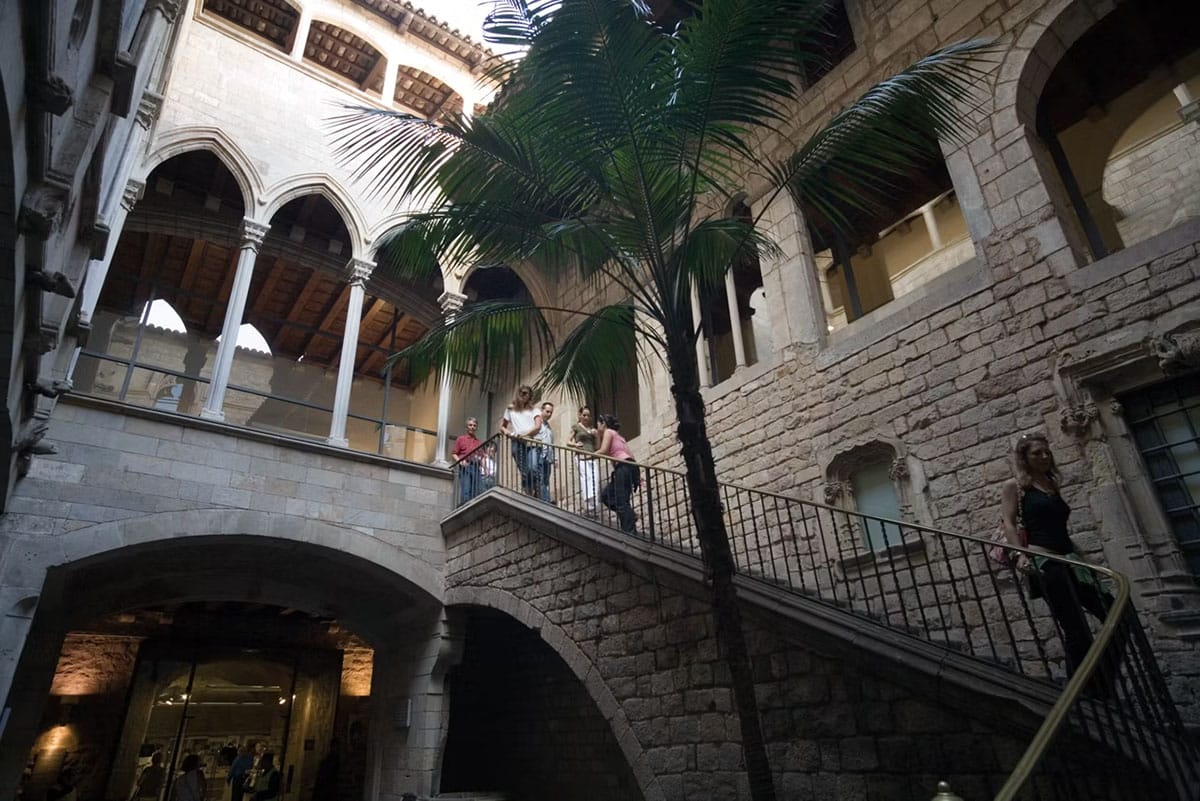 people climbing a stone staircase leading to a building with a palm tree.