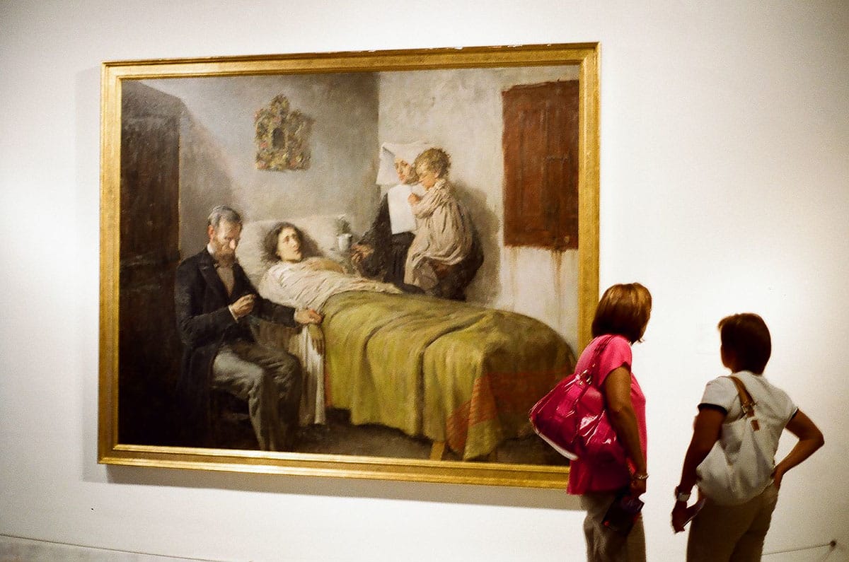 two women looking at a framed painting hanging on a wall.