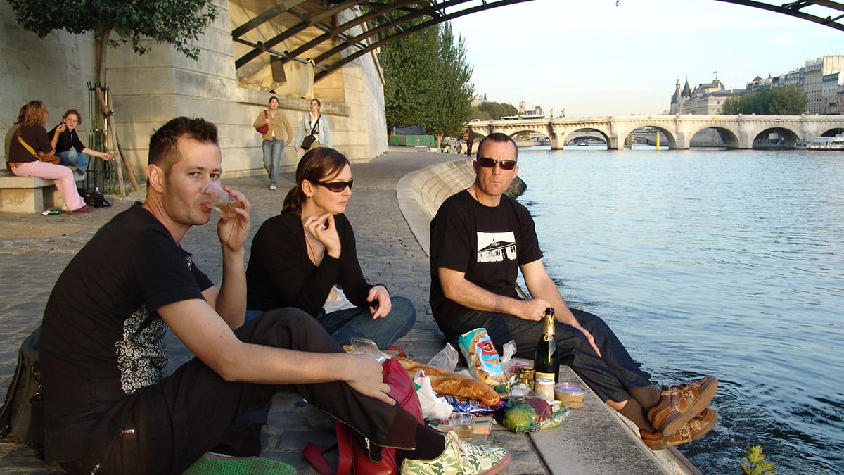 two men and a woman sitting on the banks of the Seine having a picnic.
