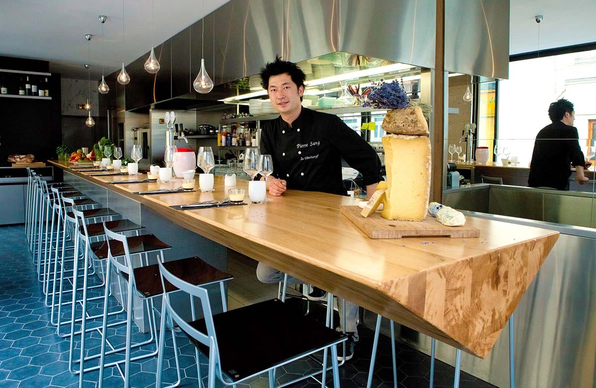 chef sitting at a wooden bar with high stools.
