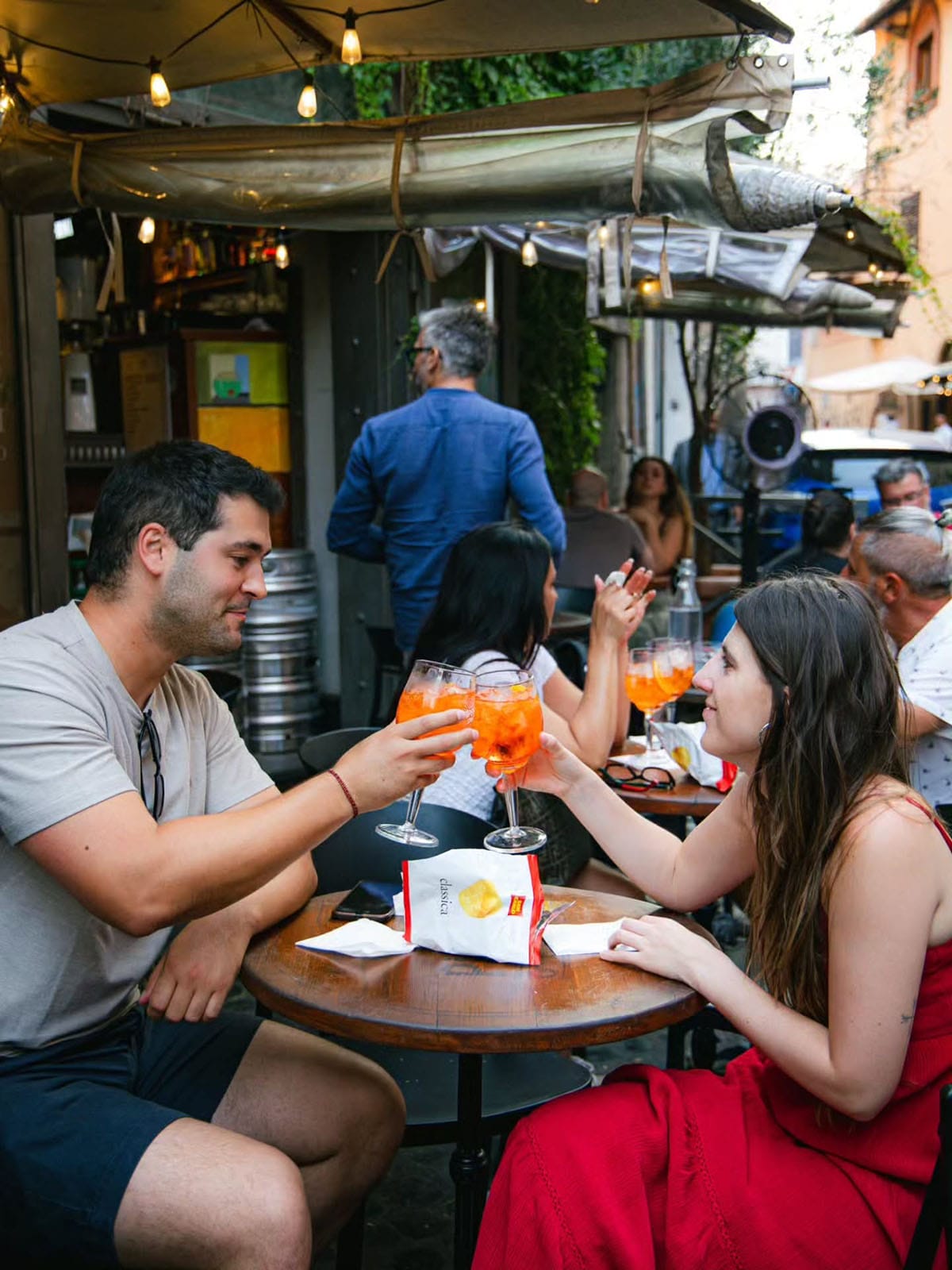 man and woman toasting with Aperol spritzes outdoors in Rome.
