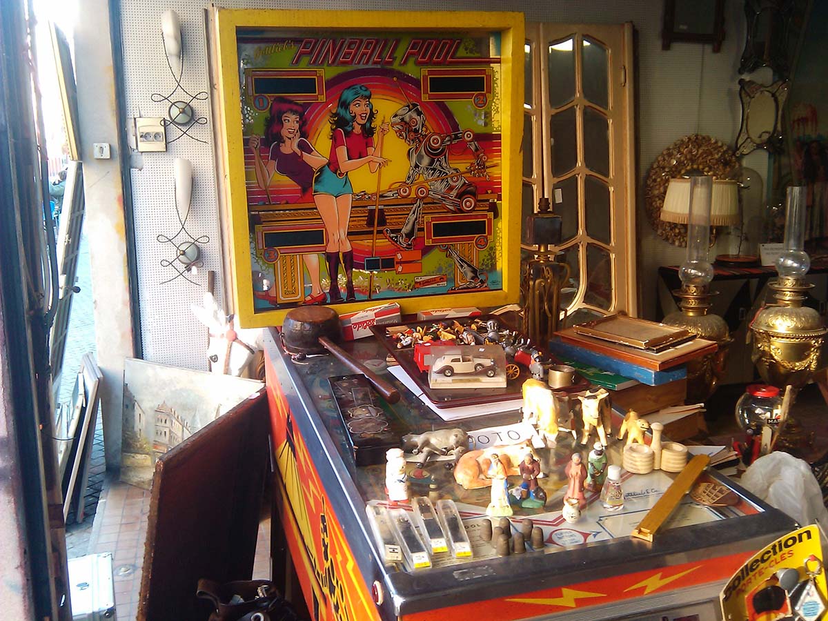 pinball machine covered with knickknacks in an antique shop.