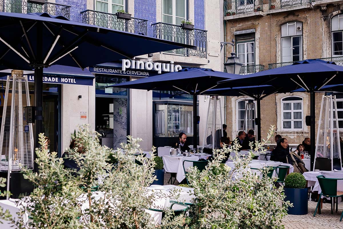 white-covered tables and chairs with blue umbrellas near a restaurant.