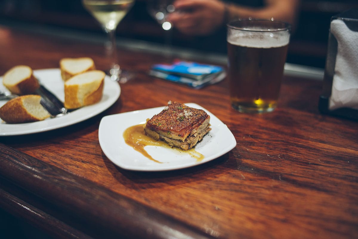 small plates of fish and sliced bread on a wooden table with a martini and small glass of beer.