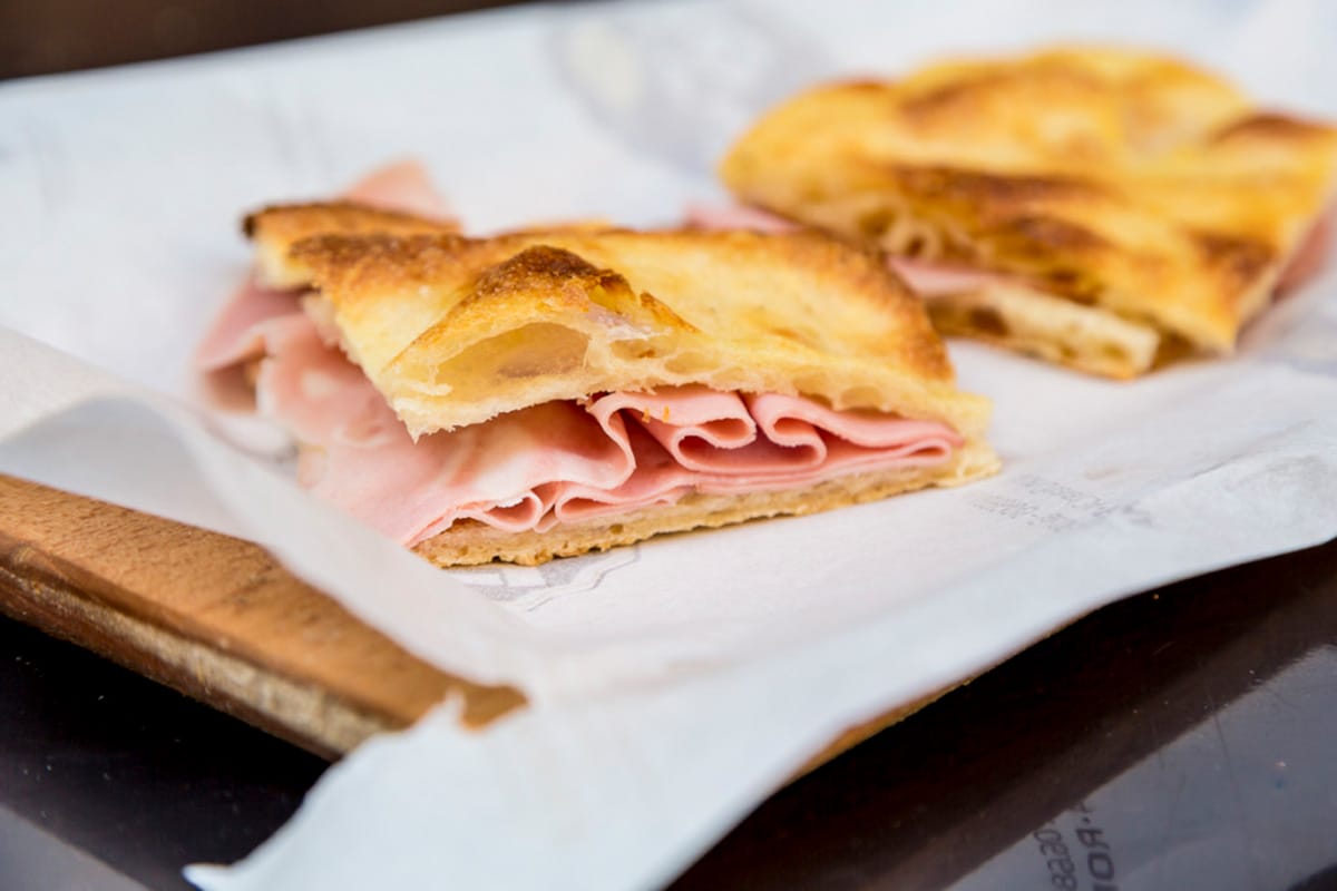 squares of pizza dough stuffed with thinly sliced mortadella on parchment paper.
