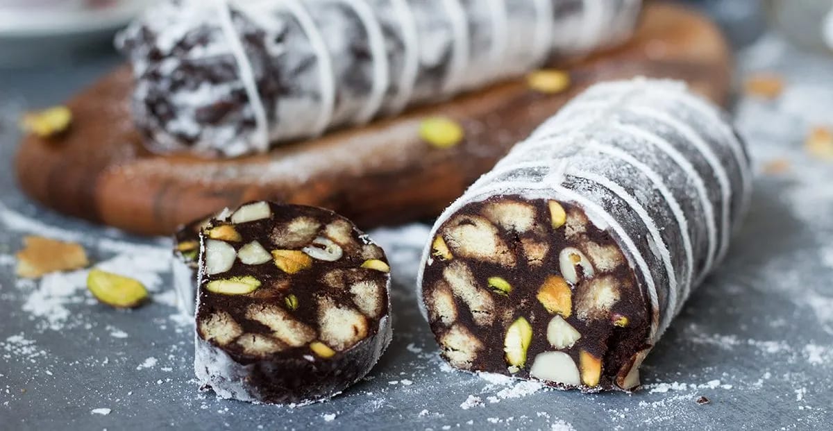 chocolate salami with nuts sliced on a gray table.