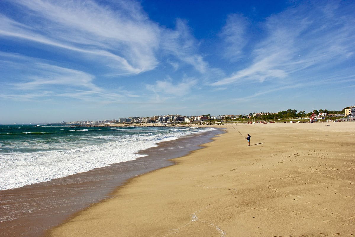 lone man fishing on a yellow sand beach in Portugal.