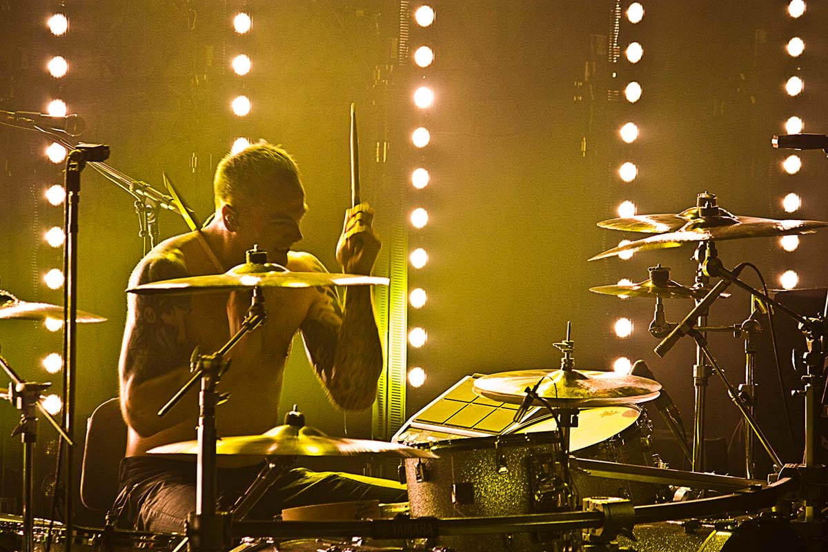 man drumming passionately onstage with yellow lighting.