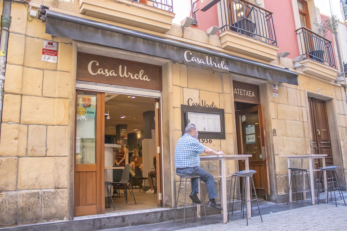 man sitting at a table outside of a restaurant in a stone building.