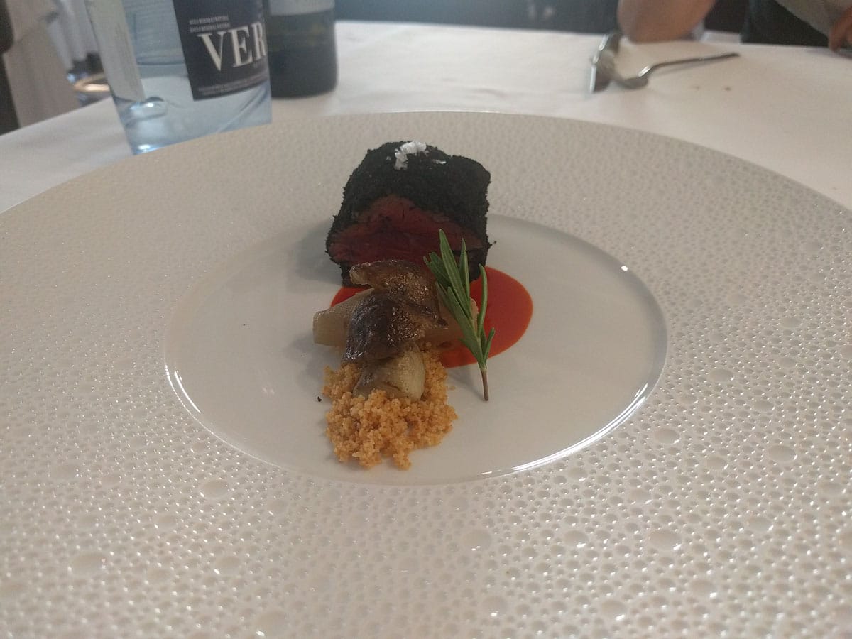 large white plate with a piece of meat garnished with sauce, breadcrumbs, and herbs.