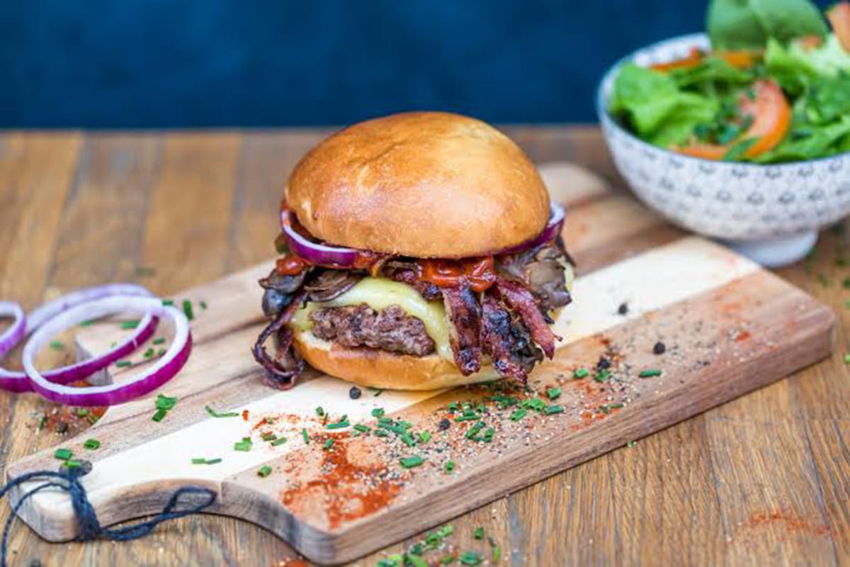 burger on a wooden cutting board with a bowl of salad.
