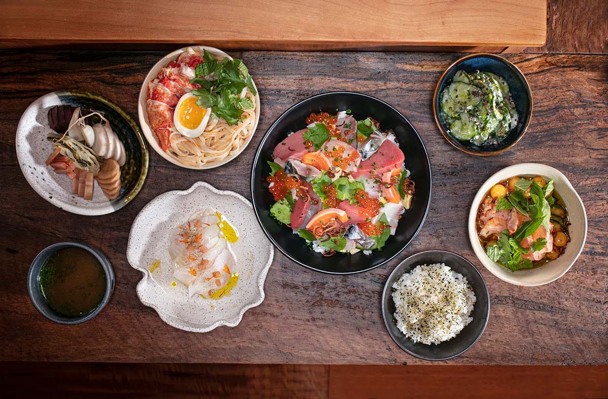 bowls of Japanese food and sashimi on a wooden table.