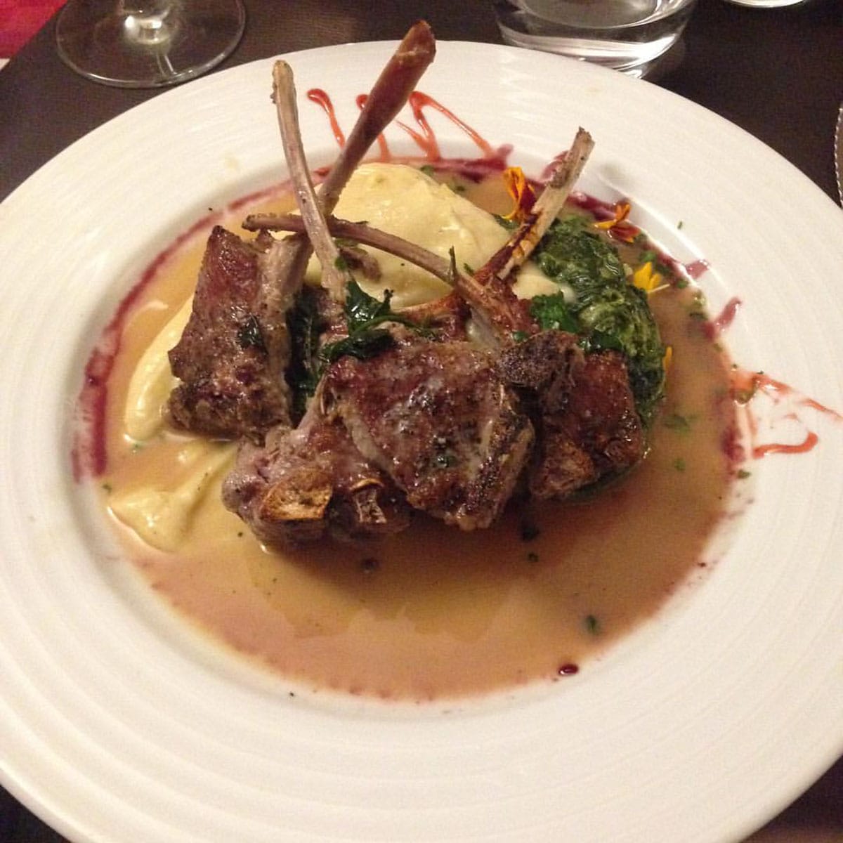 sophisticated lamb chops in a sauce on a shallow white plate.