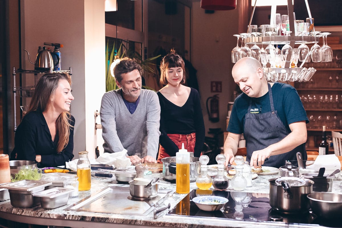 chef preparing food with three people watching.