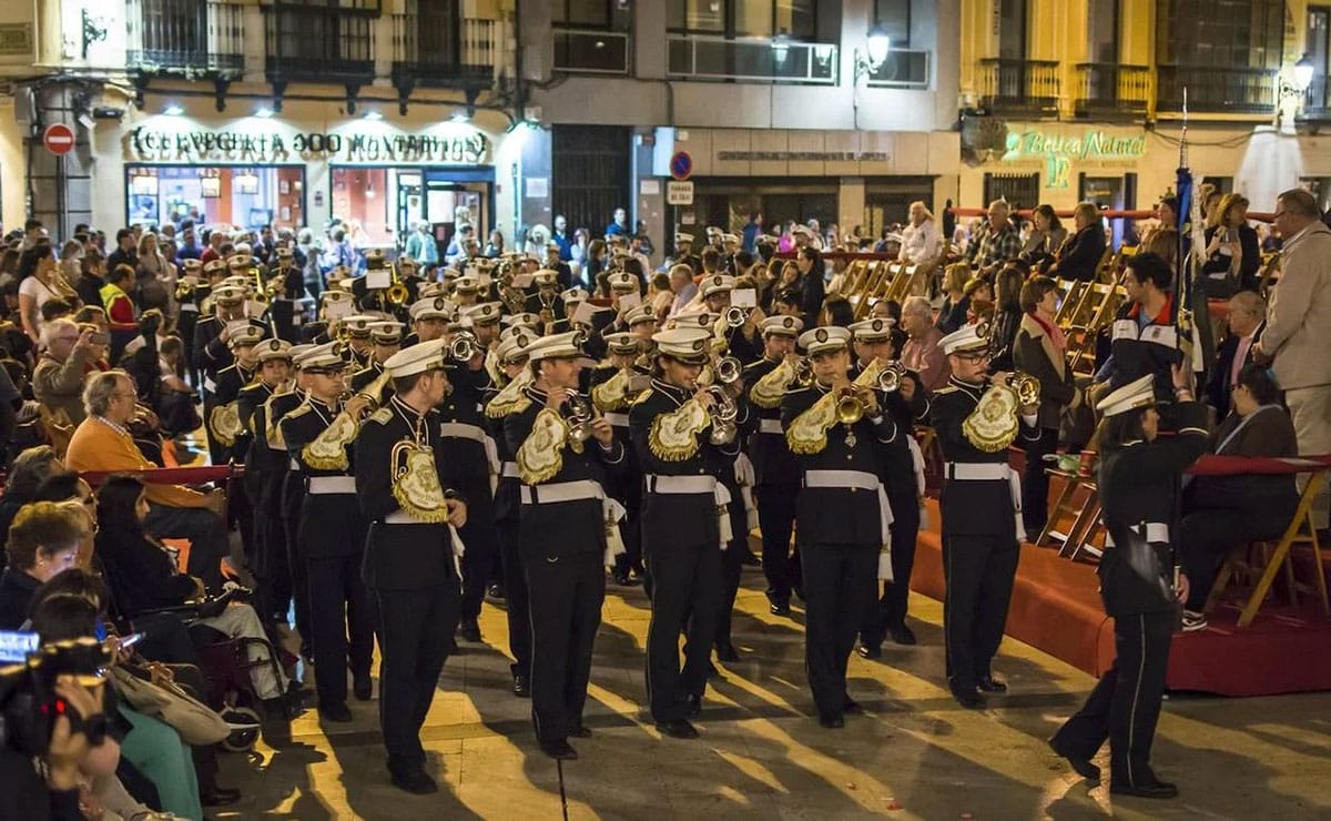 band dressed in uniforms and playing music on horns as they walk down the street.