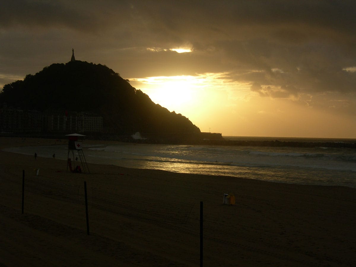 sunset behind a mountain with a beach in the foreground.