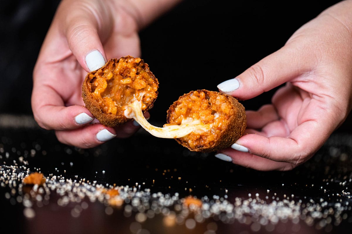 person pulling a fried rice ball apart showing melted cheese inside.