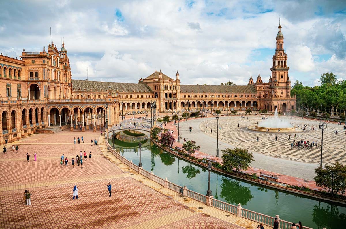 square with a river and buildings with blue sky and clouds overhead.