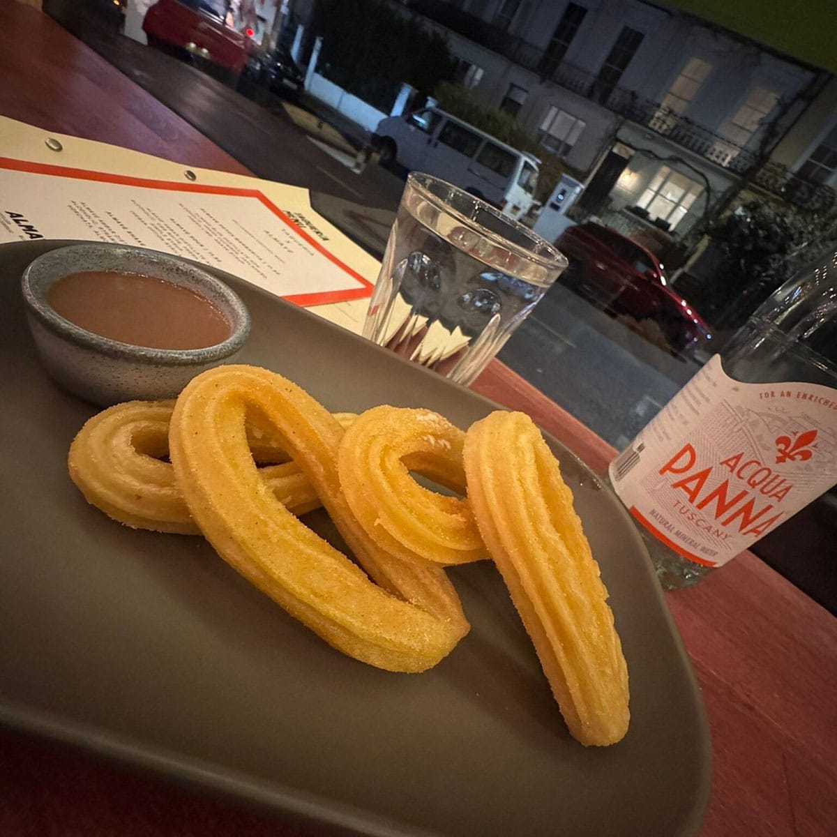 plate of churros with a bowl of dipping syrup on a table.