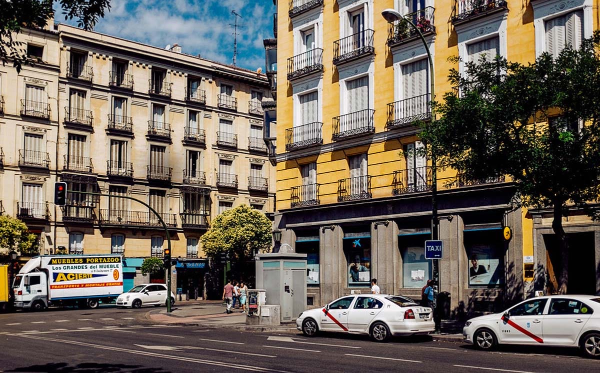 two white taxi cabs parked on the side of the road near a large yellow building.