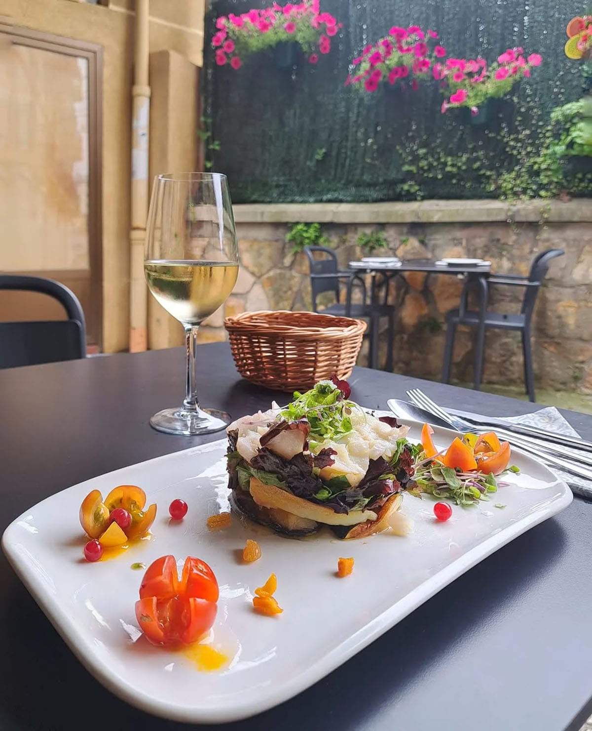colorful vegetarian food on a white platter with a glass of white wine on a black table.