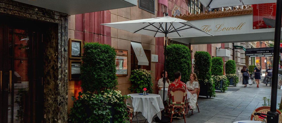 three people sitting at a round table outside of a fancy hotel in New York City.