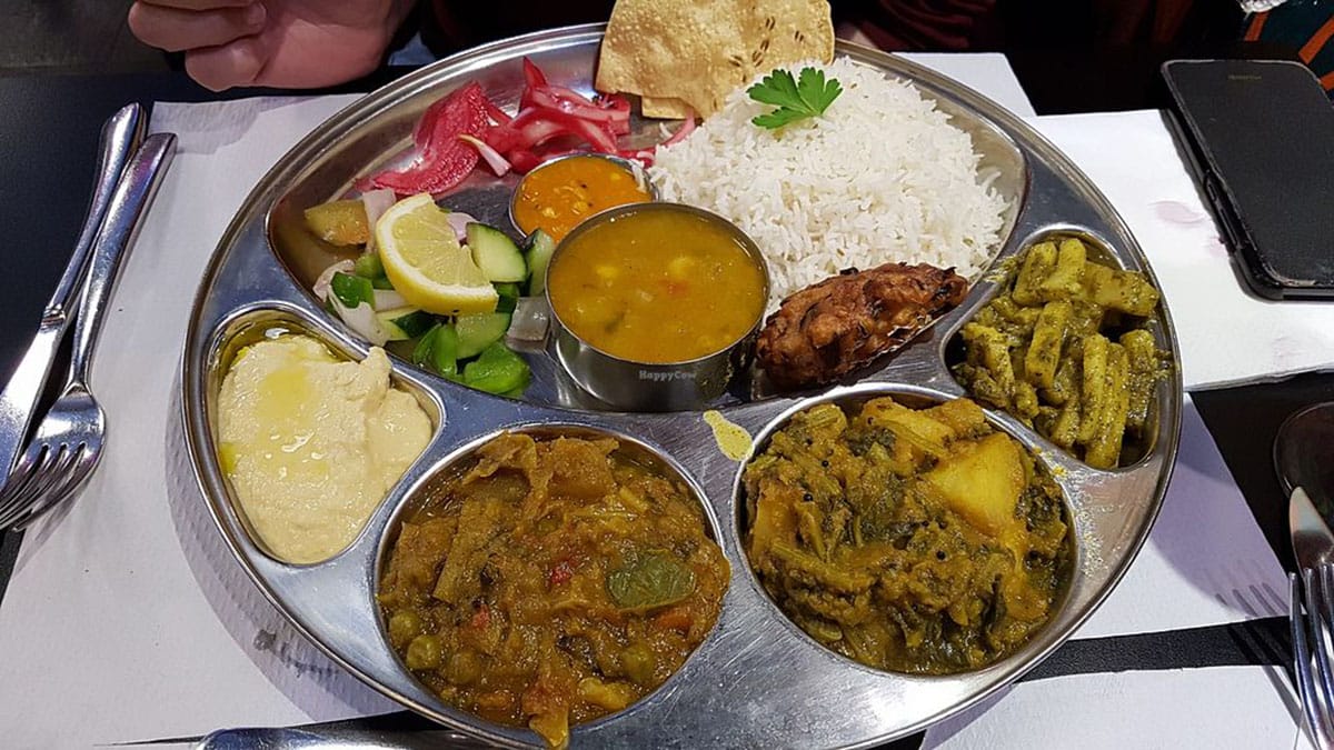 large stainless steel platter filled with rice, curry, hummus, and other vegan food.