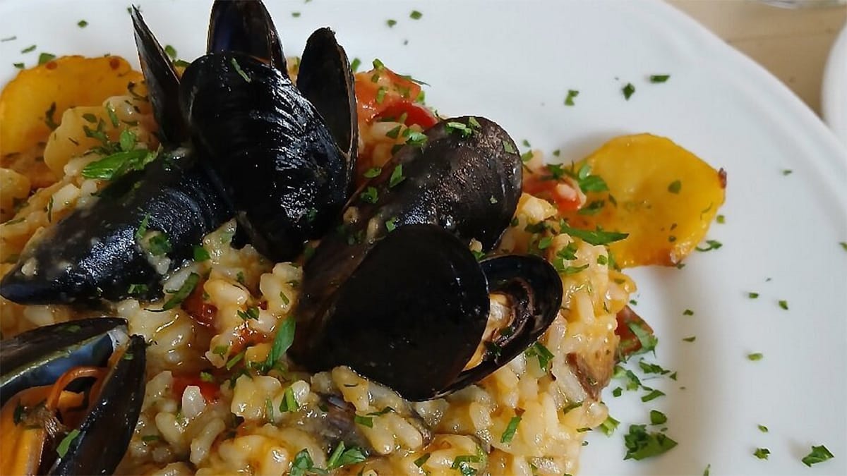 plate of rice and mussels in a sauce.