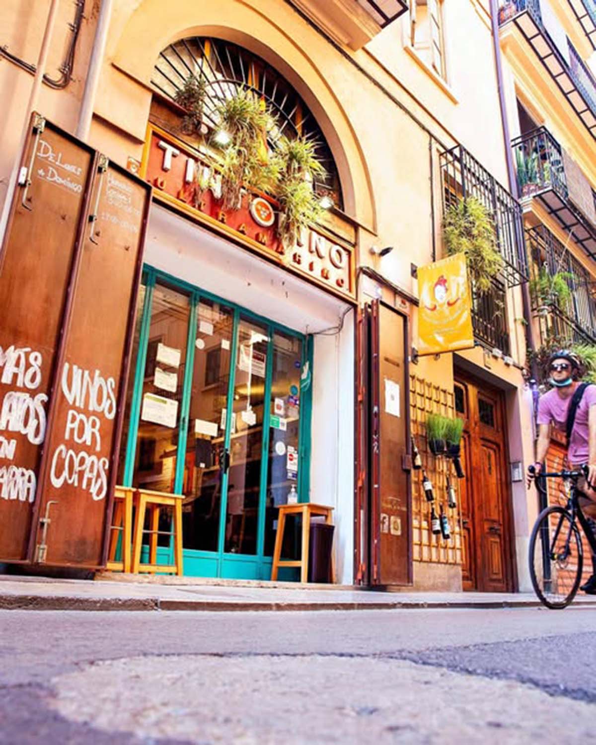 man riding a bicycle in front of a tall doorway for a wine bar and restaurant.