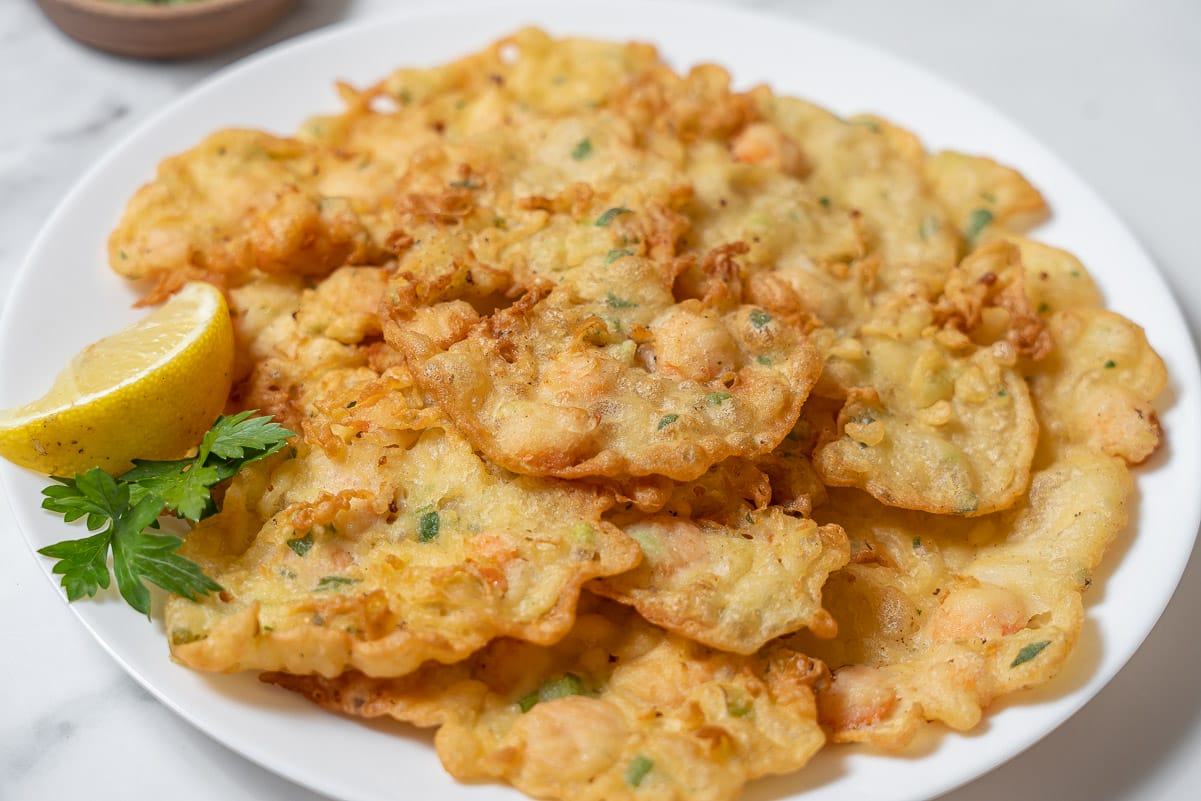 white plate of shrimp fritters paired with a lemon wedge and parsley sprig.