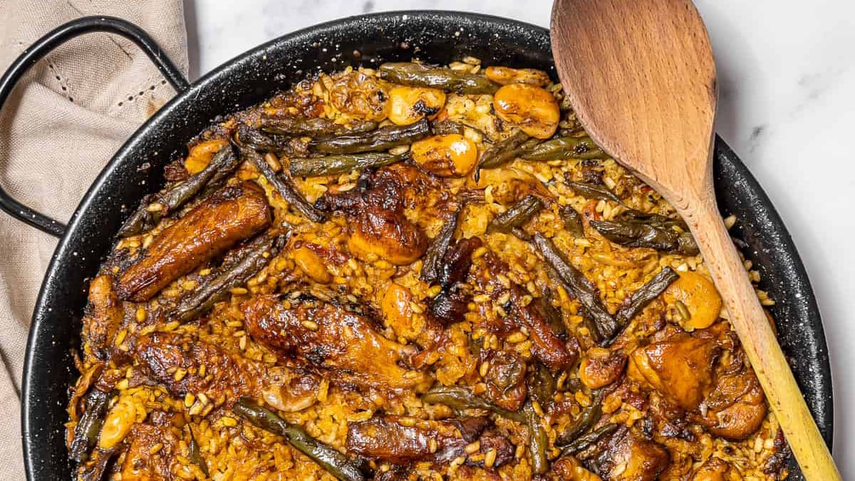 wooden spoon laying across a pan of paella with a linen napkin.