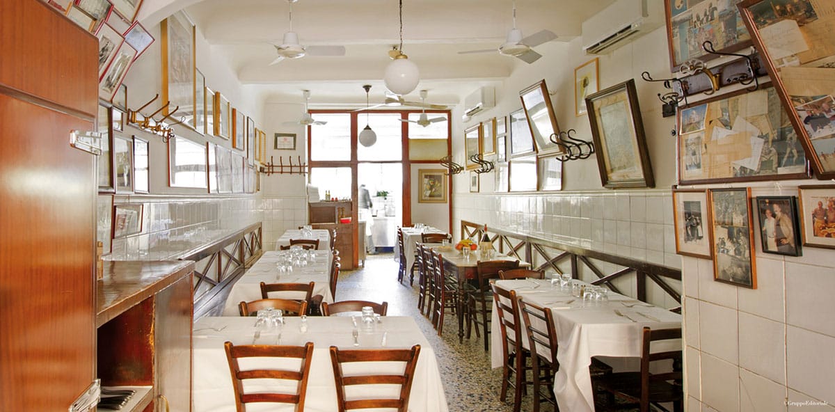 small tables with white tablecloths inside a white tiled room.