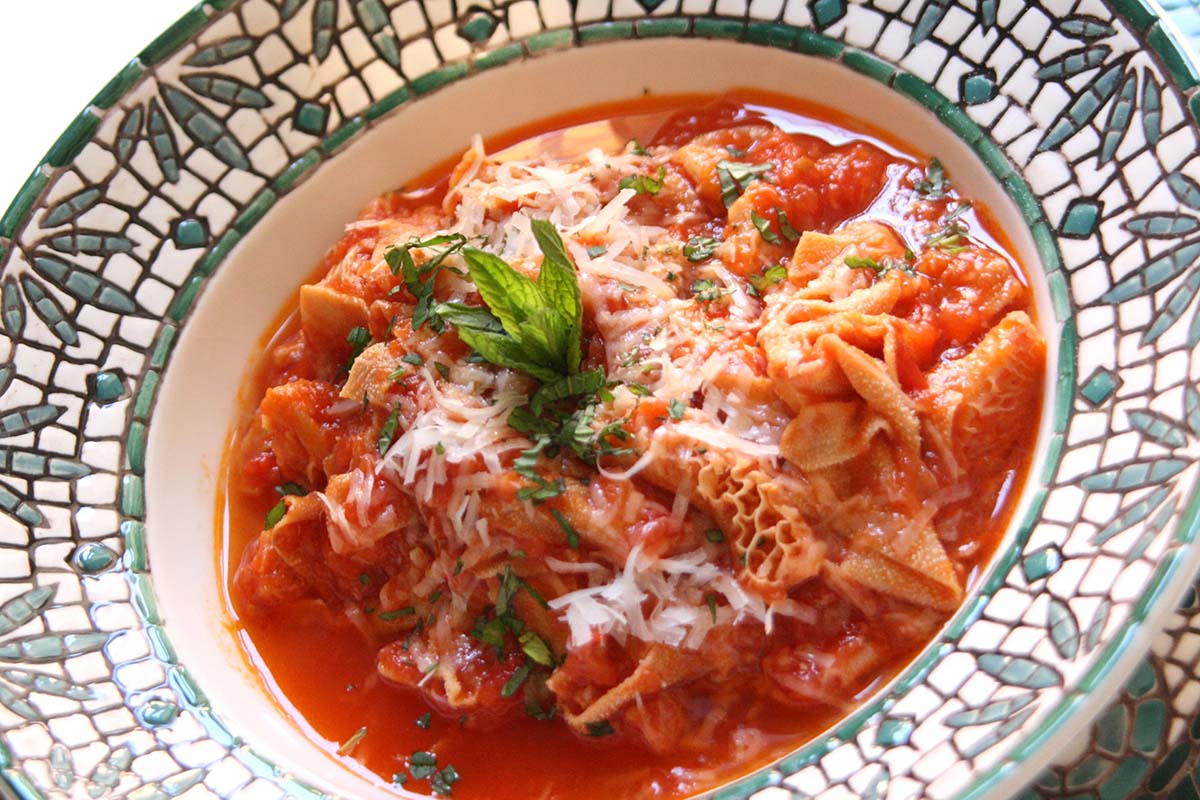 mosaic-painted ceramic dish filled with trippa alla romana garnished with mint.