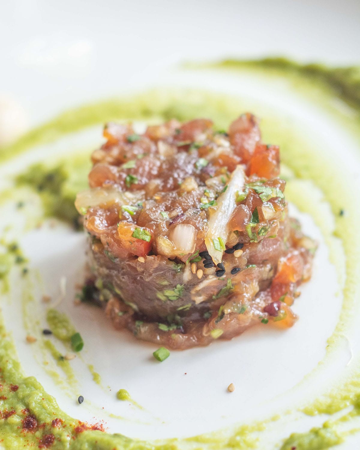 tuna tartare on a plate with an avocado sauce around it.