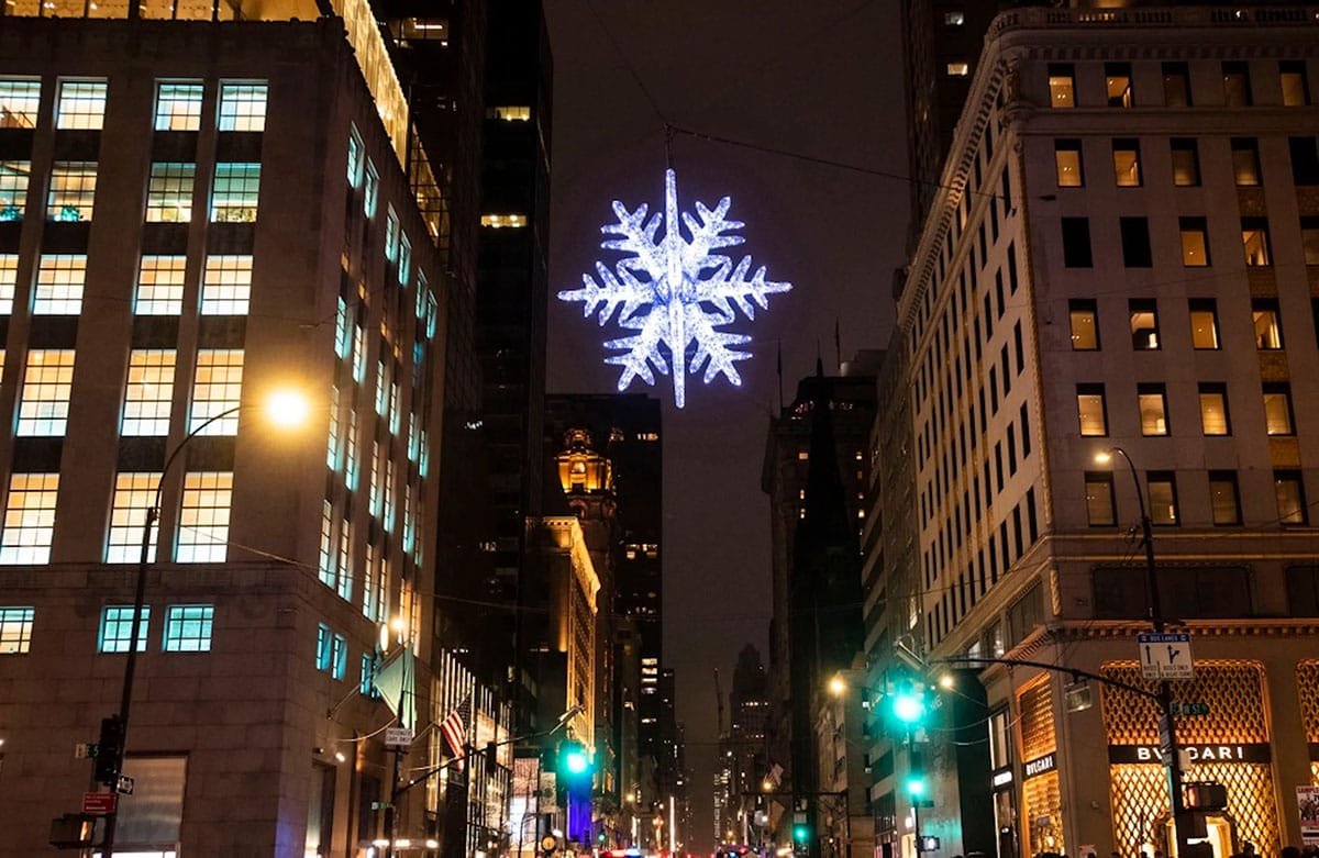 large snowflake hanging from wires at a busy intersection.