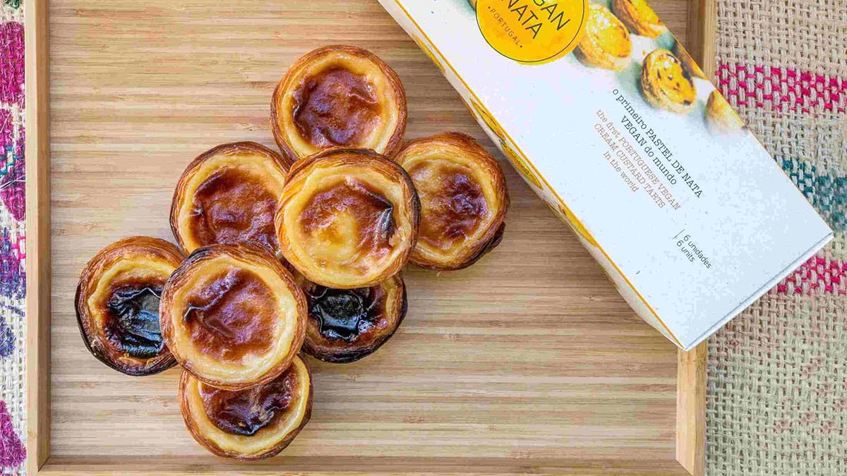 stack of vegan custard tarts on a wooden tray with a box of tarts nearby.