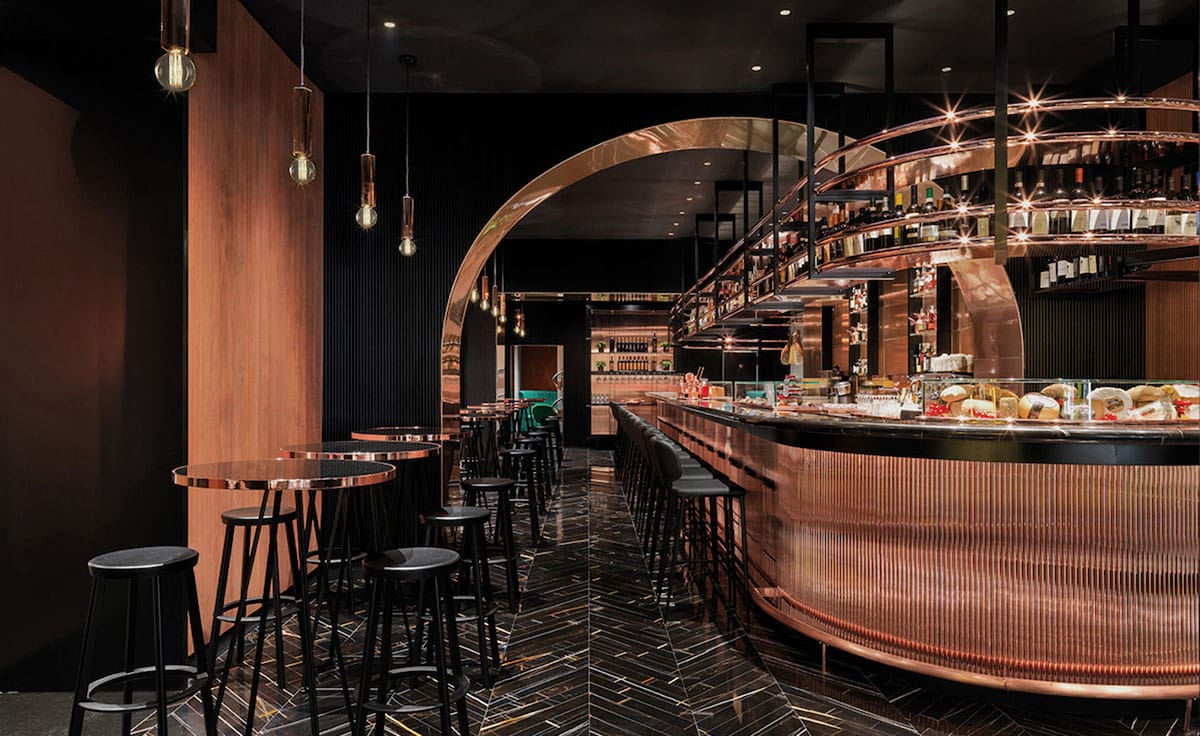 tables and stools near a bar with an arched entrance and classy lighting.