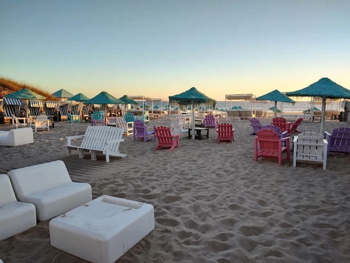 colorful wooden chairs and straw umbrellas on a sandy beach.