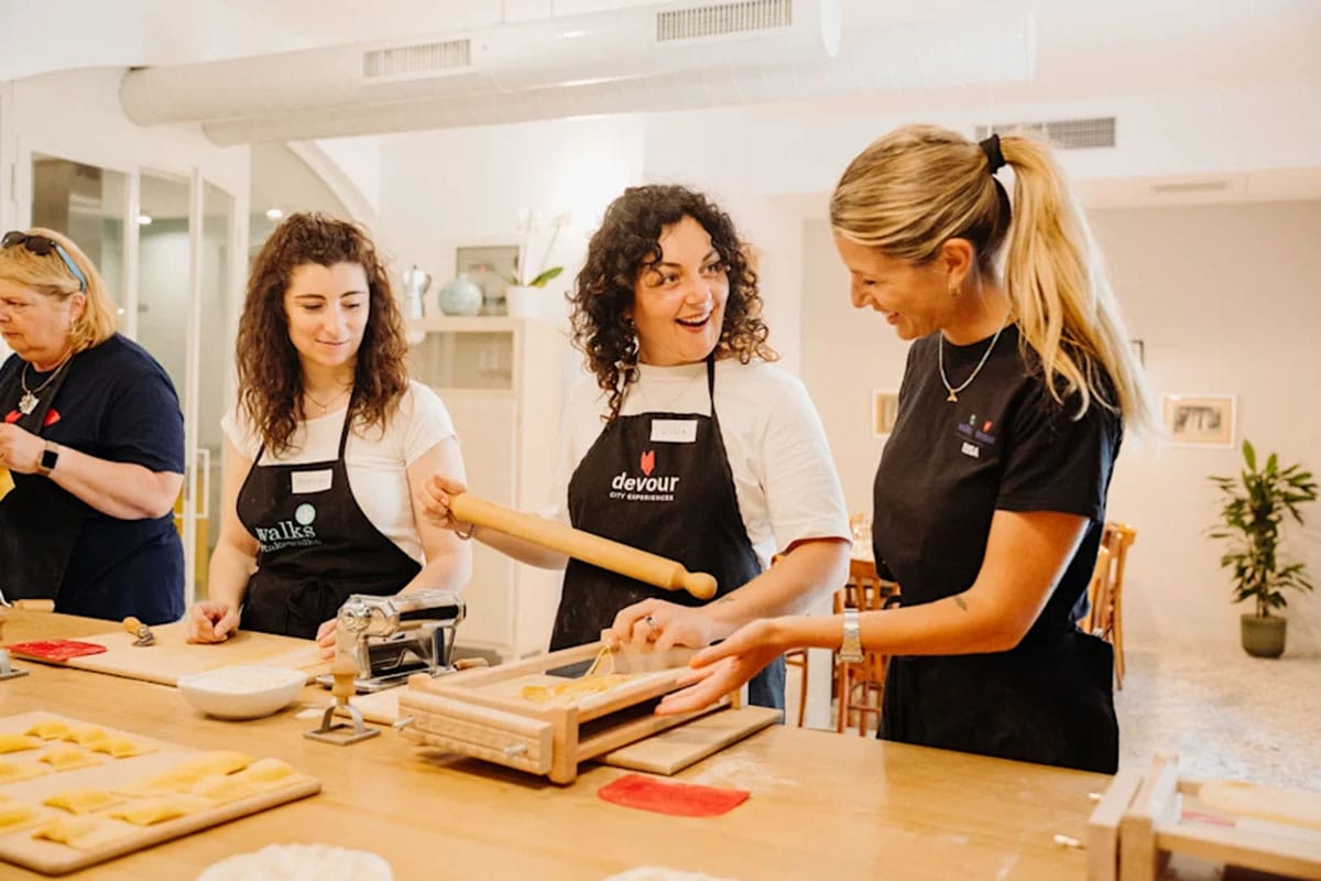 ladies wearing black aprons making pasta at a wooden table.