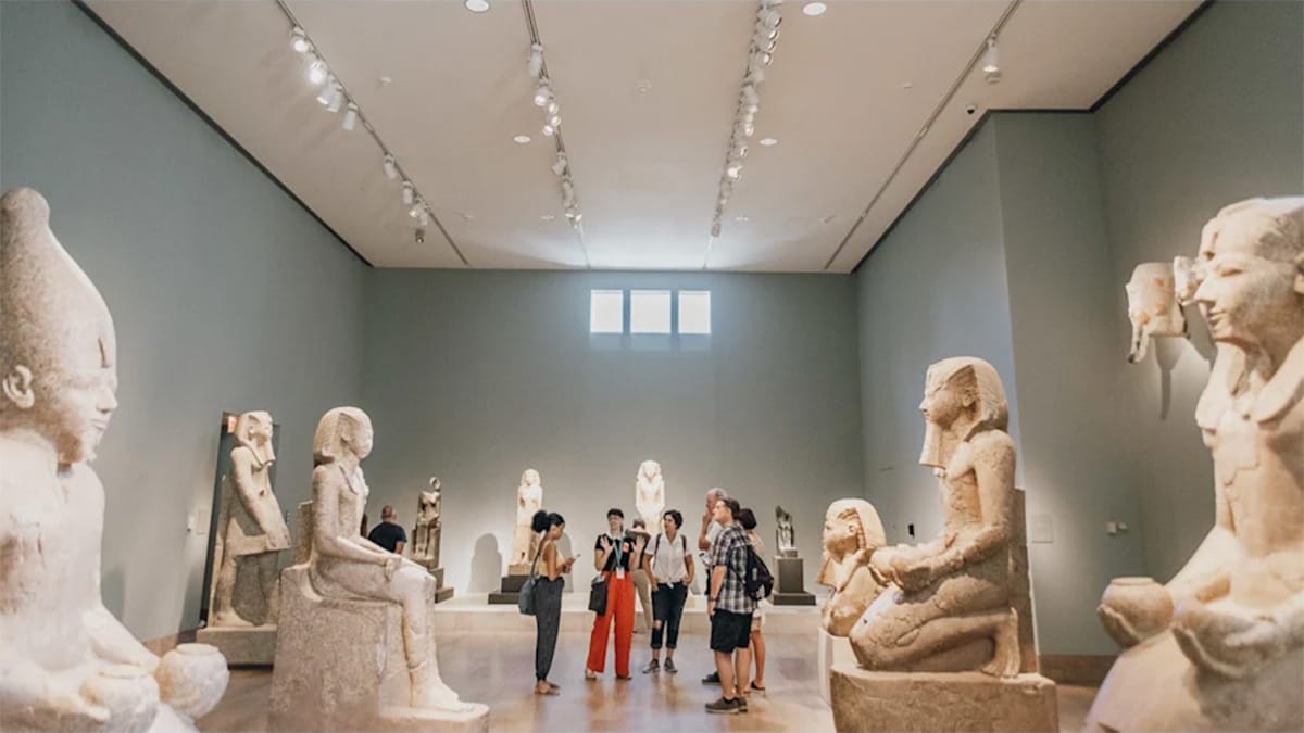 tour guide leading a small group through an art gallery with large white sculptures.