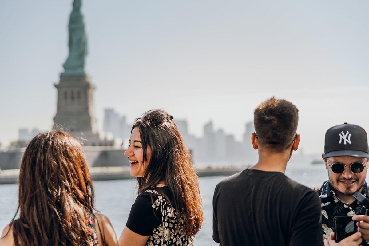 group of people talking as they look at the Statue of Liberty.