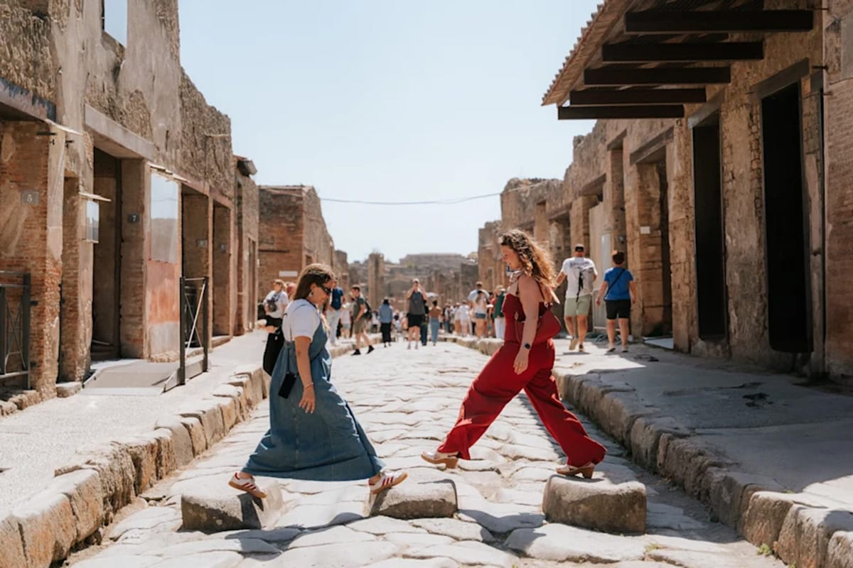 two ladies stepping on stones across a street in Pompeii.