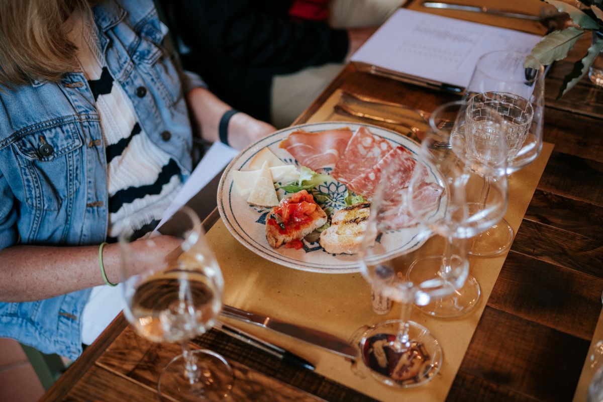 A plate of Italian bites on a ceramic plate next to glasses of wine.