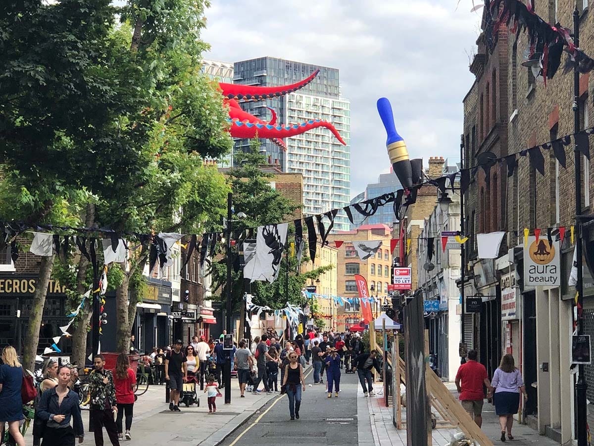 London street with trees down the center and skyscrapers in the background.