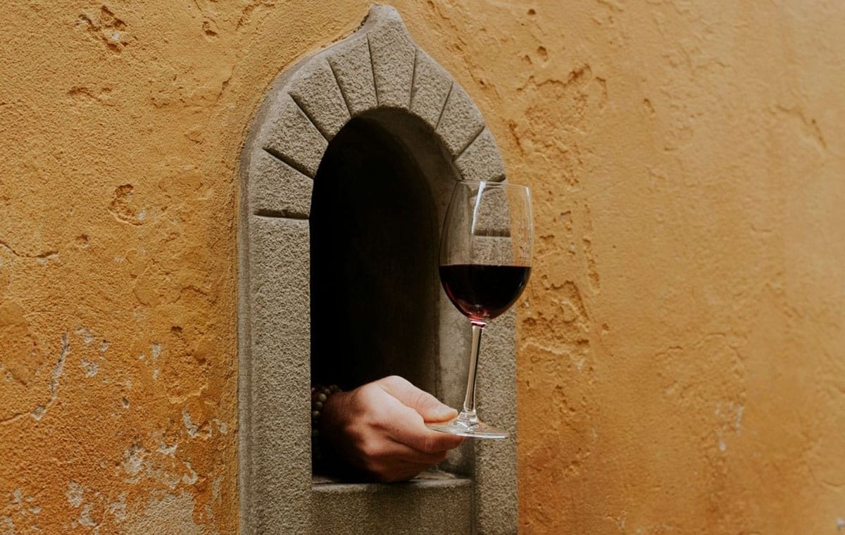 person holding a wine glass out of a small wine window in Florence.