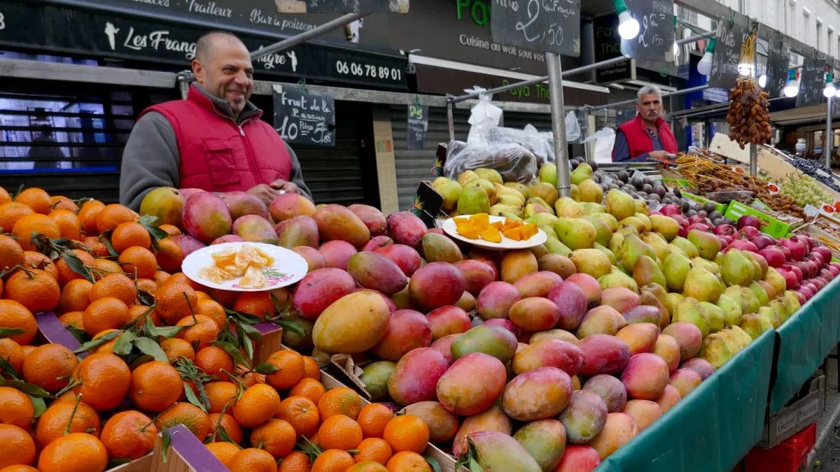 men selling fresh fruit in outdoor stands at a French market.