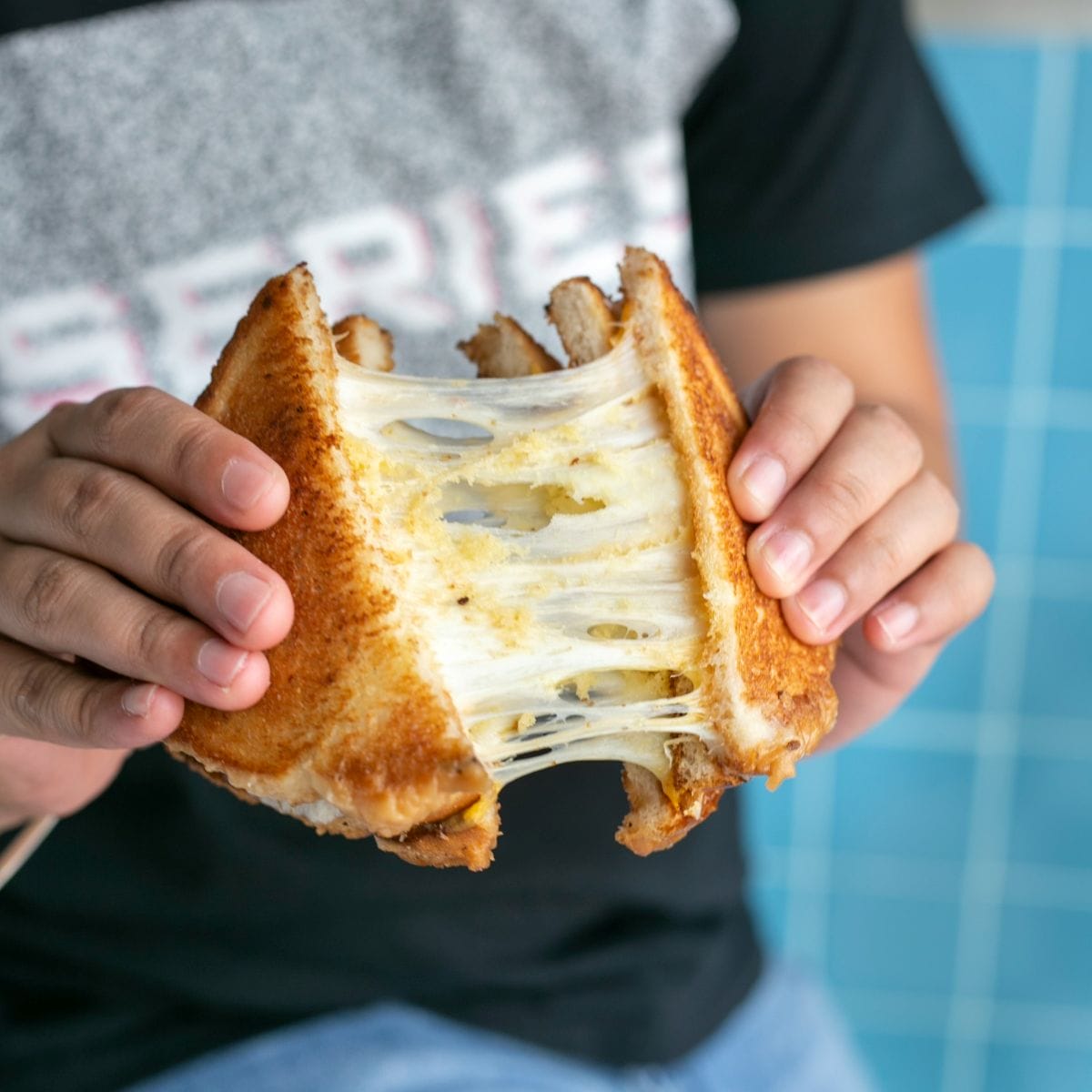 A person pulling apart a cheesy bikini sandwich.
