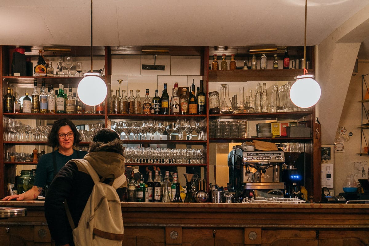 shelves of glasses and bottles behind a wooden bar.